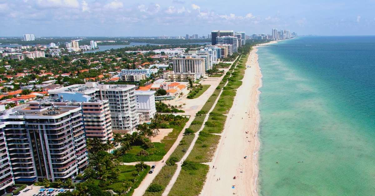 Image of the main beach front in Florida, featuring an aqua coloured ocean and tall sea-facing buildings.